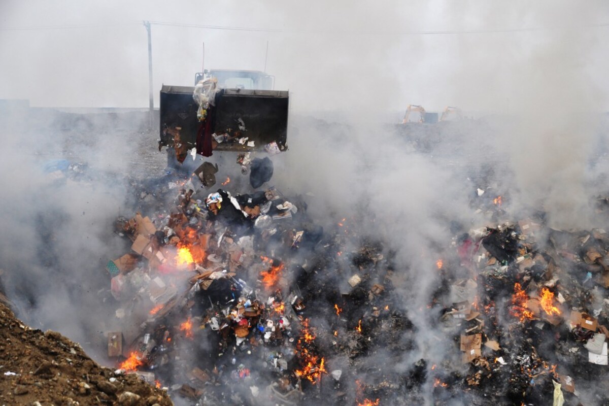 A loader pushing refuse onto a burning military burn pit in Iraq, heavy smoke plume rising