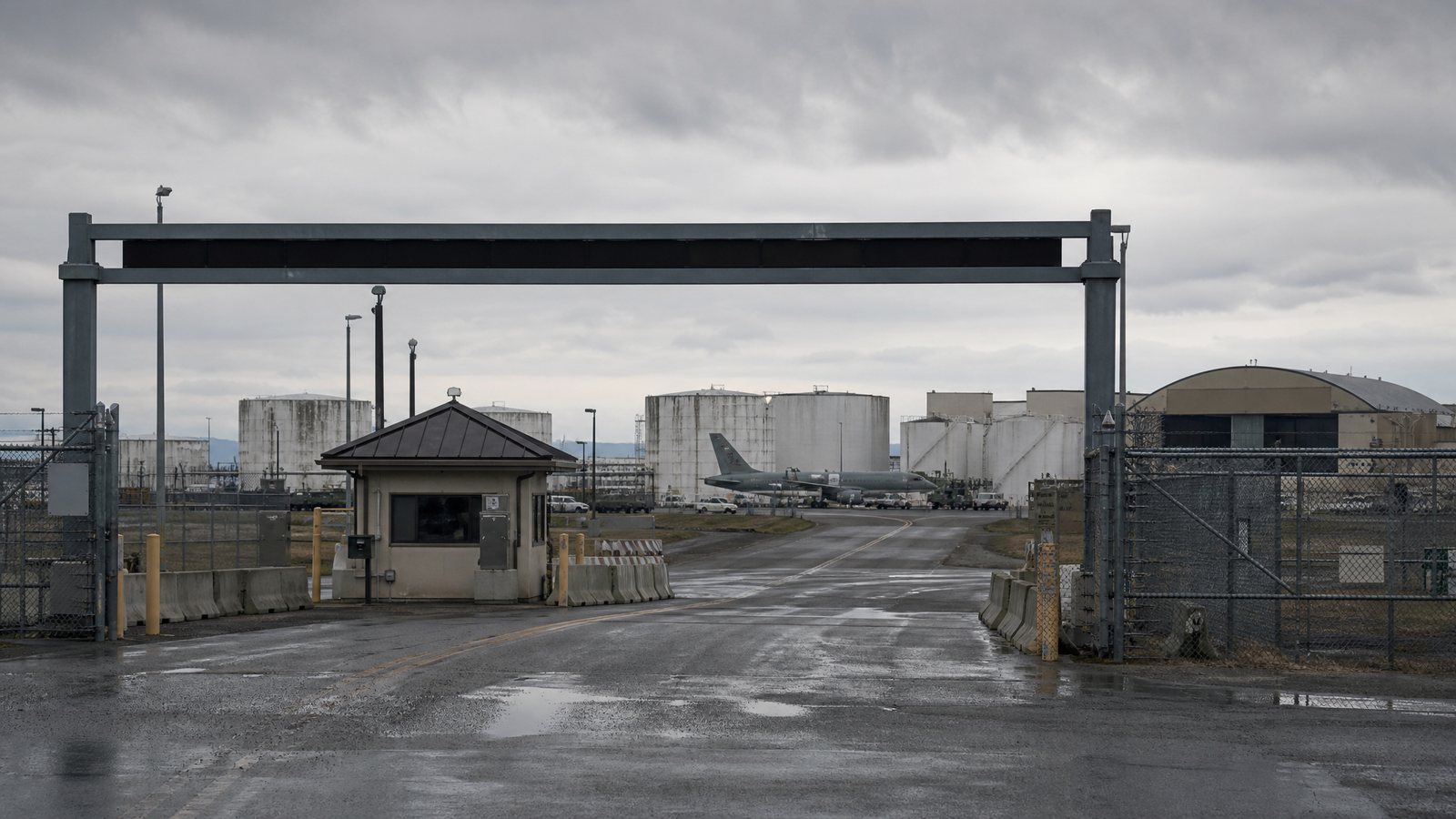 The main gate of a military installation looking toward bulk fuel storage tanks, aircraft and hangars on the flight line