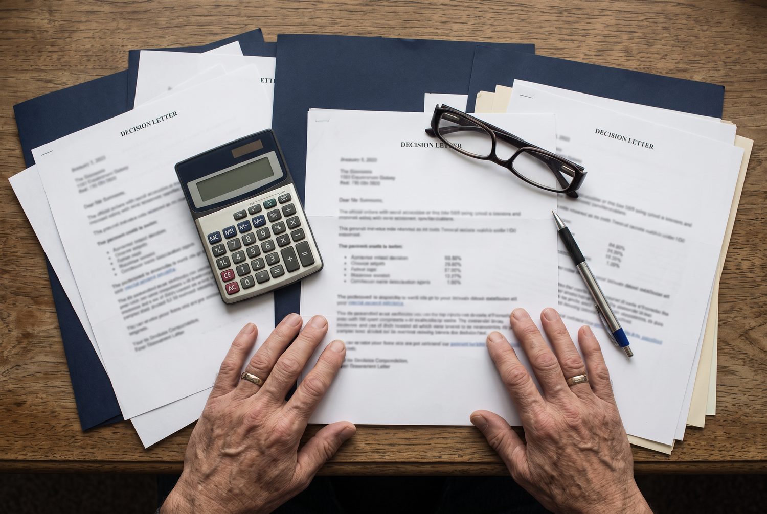 Stacked VA decision letters with a calculator, reading glasses and a pen on a desk