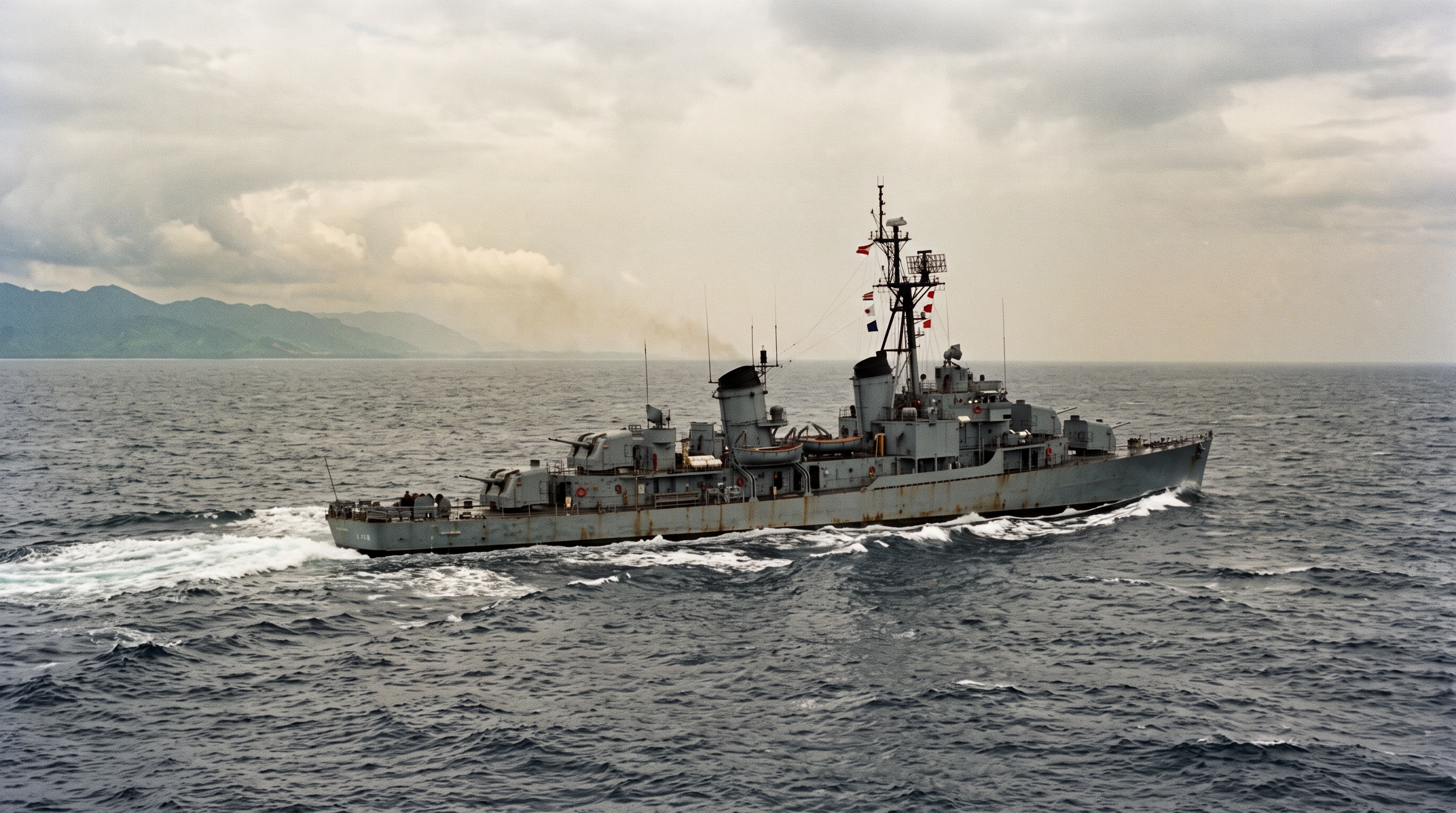 A Vietnam-era haze-gray destroyer under way in coastal waters with the Vietnamese coastline a faint line on the horizon